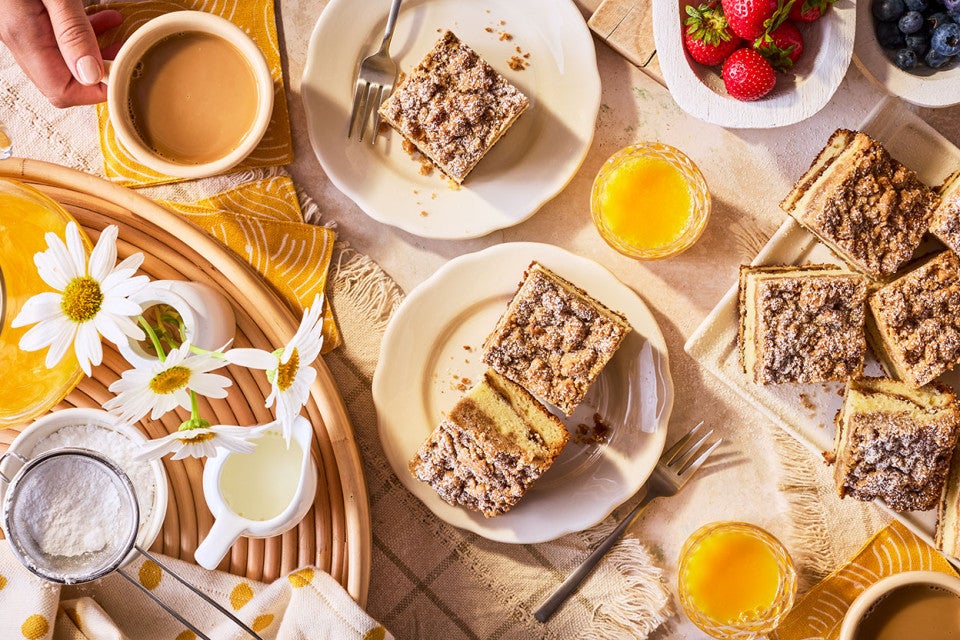 A table arranged with slices of Our Favorite Sour Cream Coffee Cake and other breakfast items.