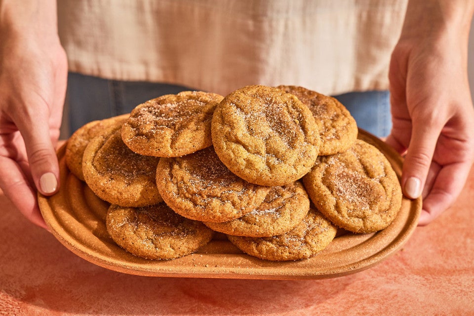 Pumpkin Snickerdoodle Cookies stacked and arranged on a plate with someone holding the plate up