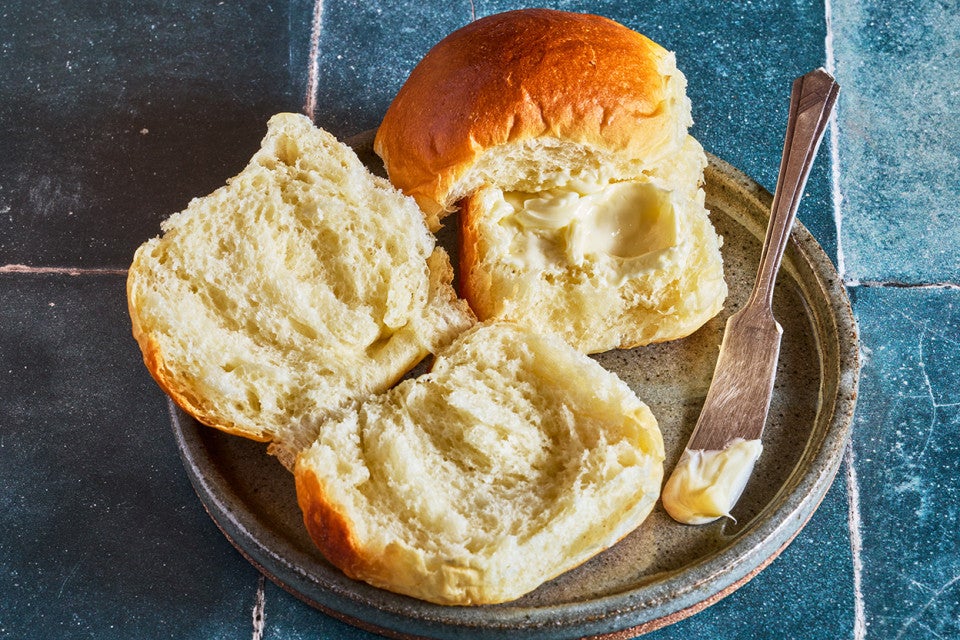 Milk bread rolls on a plate with one opened and buttered