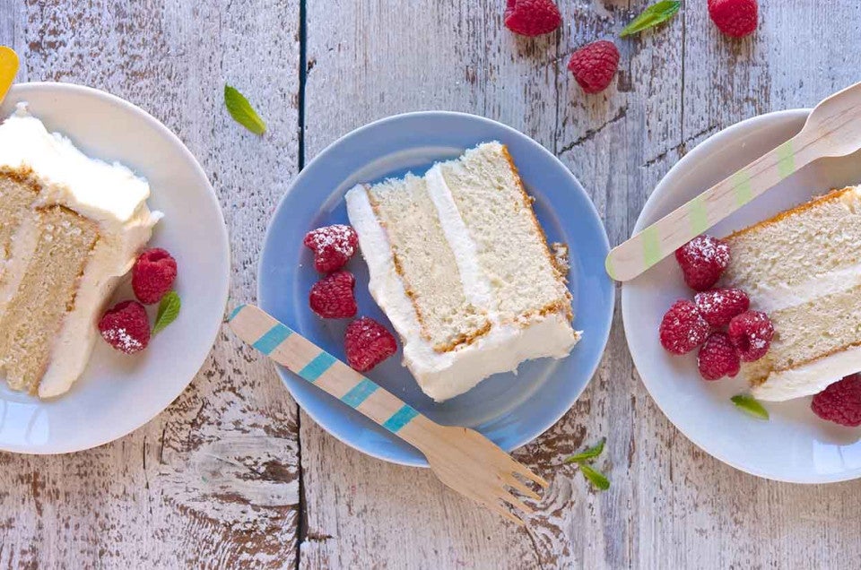 Three slices of Tender White Cake on plates, revealing their double layers of white cake and vanilla frosting.
