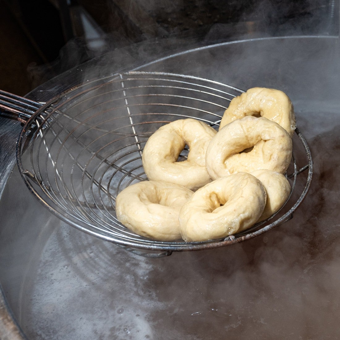 A wire ladle pulling bagels from a pot of boiling water. - select to zoom