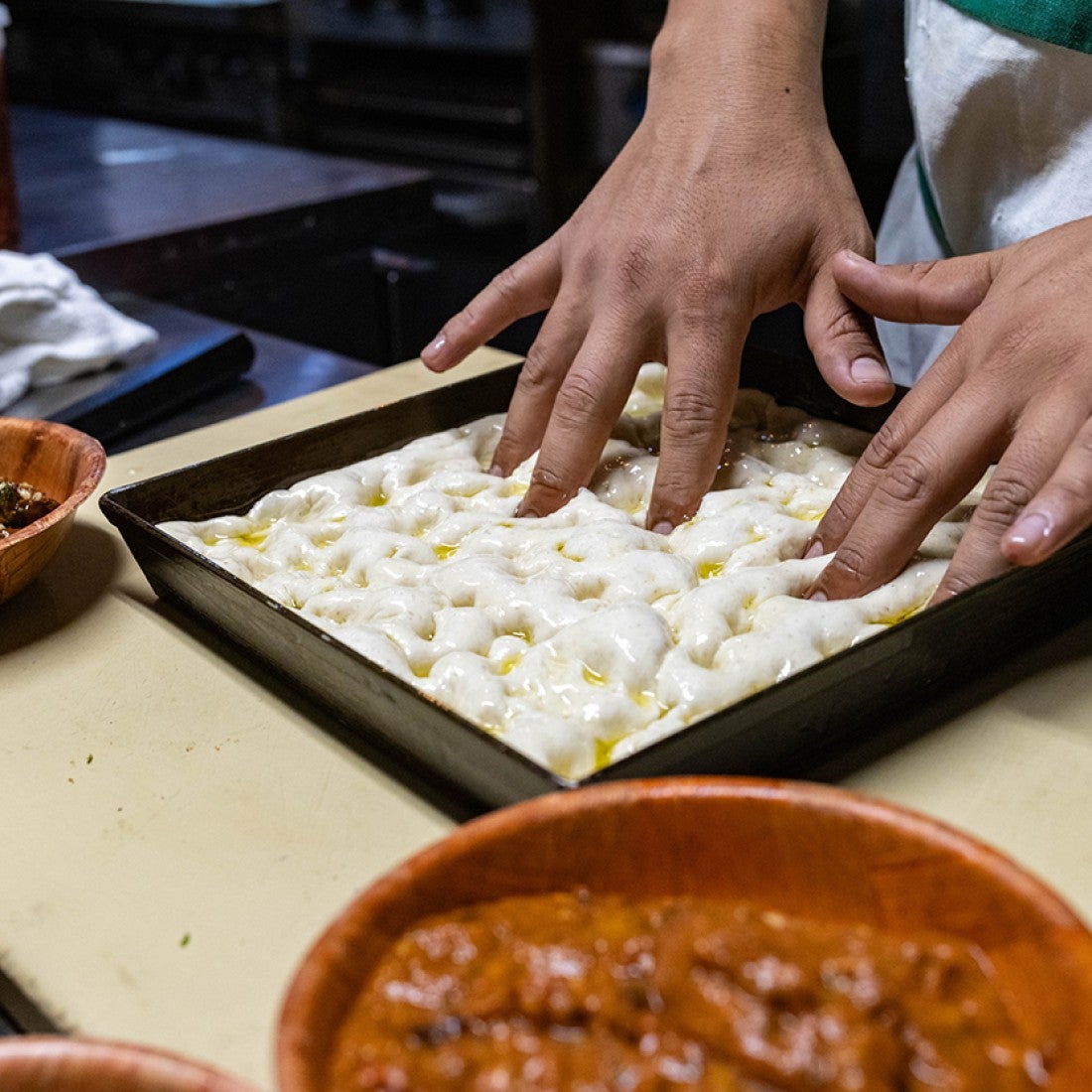 Hands kneading a tray of raw focaccia dough. - select to zoom