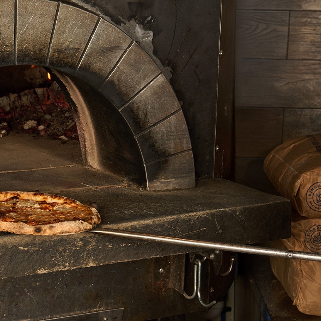 A pizza on a peel in front of a woodfired oven. - select to zoom