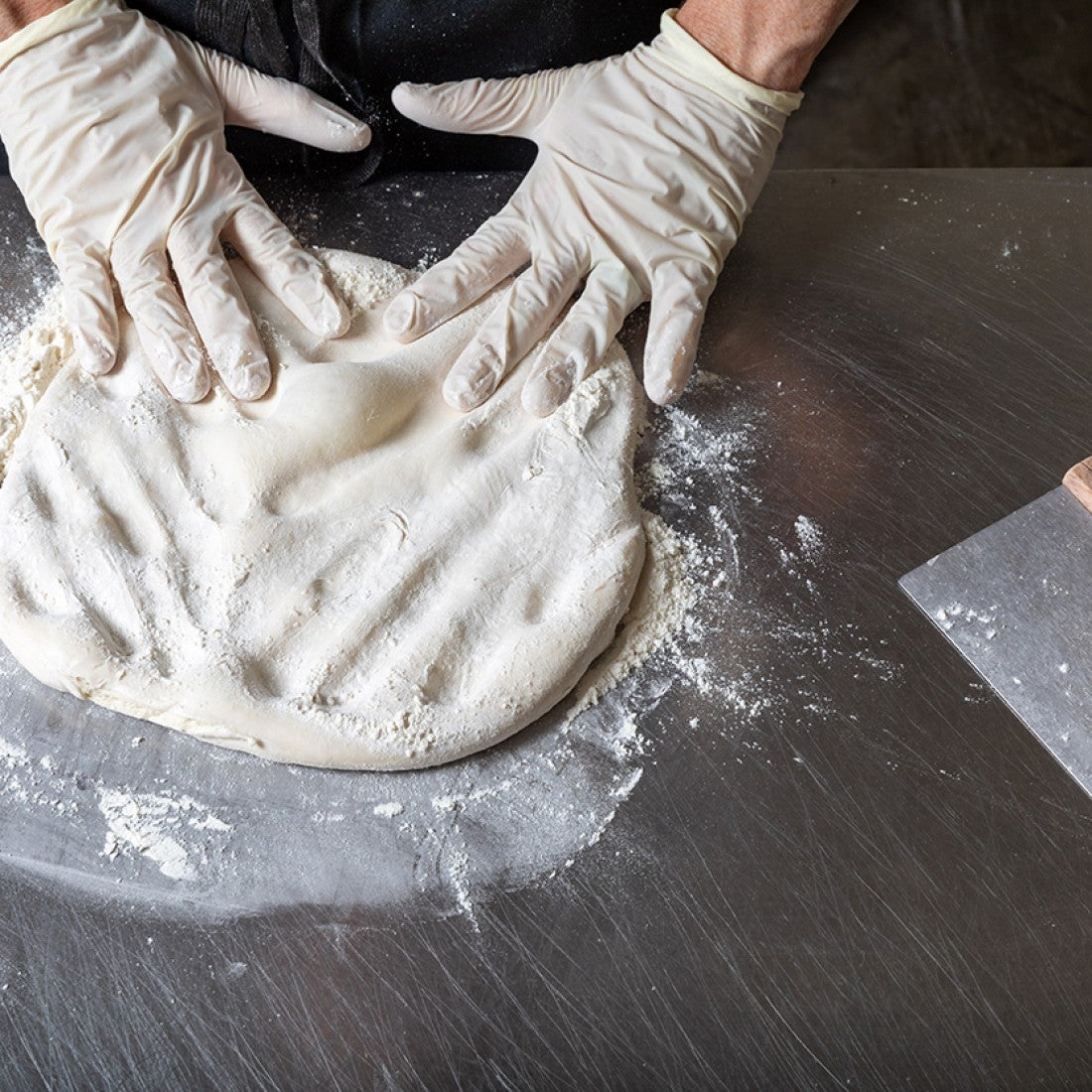 Photograph of hands kneading pizza dough that's covered in flour on a counter. - select to zoom