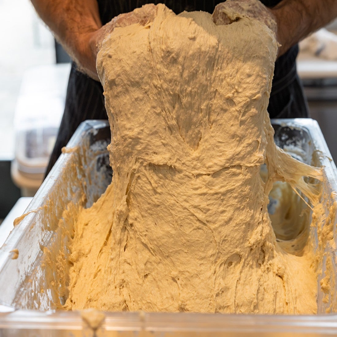 Hands pulling raw pizza dough from a container. - select to zoom