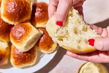 Two hands photographed pulling apart a fluffy homemade dinner roll exposing the airy and moist interior.