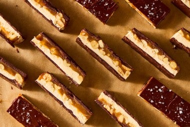 Multiple chocolate peanut nougat bars sliced and arranged on parchment paper showing the layers of chocolate, nougat, caramel, and peanuts.