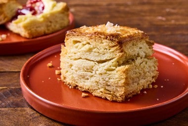 Side view of a tall ultimate flaky biscuit that clearly shows horizontal layers in the biscuit, a perfect golden baked exterior, and a bit of salt on top.
