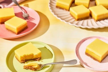 A table set with pastel colored tableware and plates with Passionfruit Bars spread out.