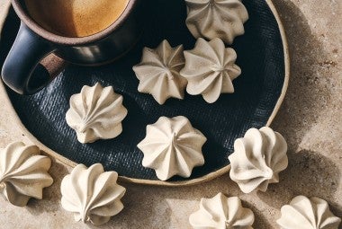 Espresso Meringues photographed from above and randomly spread on a dark plate with a cup of coffee in the upper left of the image.