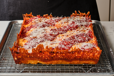 Detroit pizza on a baking rack showing the cooked pizza edges with crispy cheese and dough and a thick overall pizza.