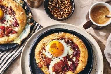 Breakfast Shakshuka shown on a plate with coffee and hot pepper flakes also in the picture.