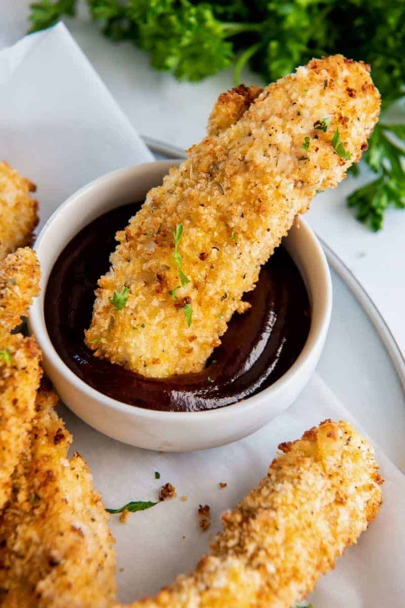Breaded air fryer chicken tenders on a white plate with parsley with buffalo sauce in the corner