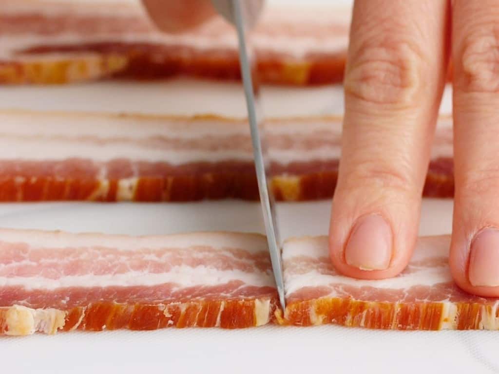 Cutting raw bacon in half with a knife