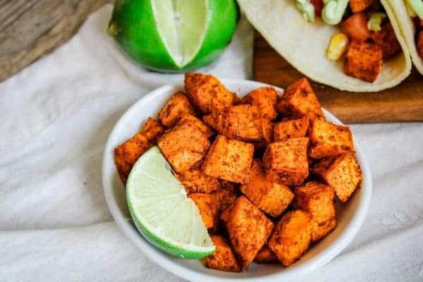 Wide angle of mexican sweet potatoes in a white bowl with a lime slice. Taco and lime showing in background