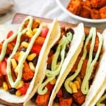 Sweet Potato Black Bean Tacos served on a rectangular wooden tray topped with avocado crema