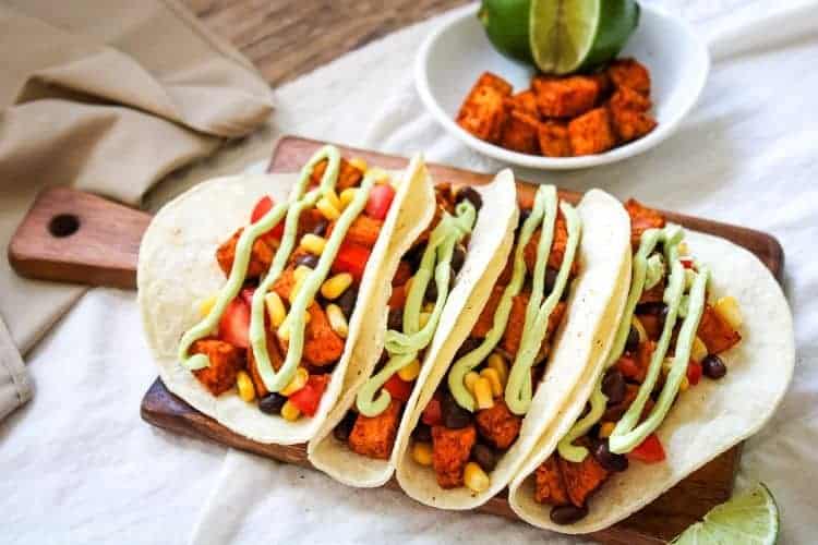Sweet Potato Black Bean Tacos on a small brown cutting board with a small bowl of mexican potatoes in back