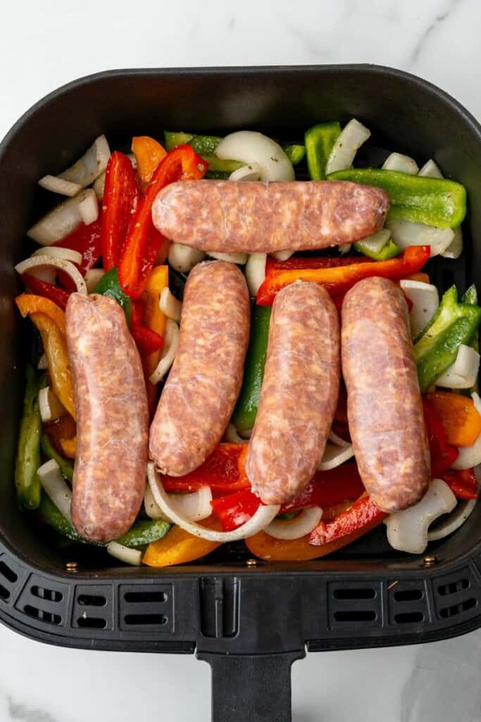 Raw italian sausages, peppers, and onions in an air fryer basket ready to cook