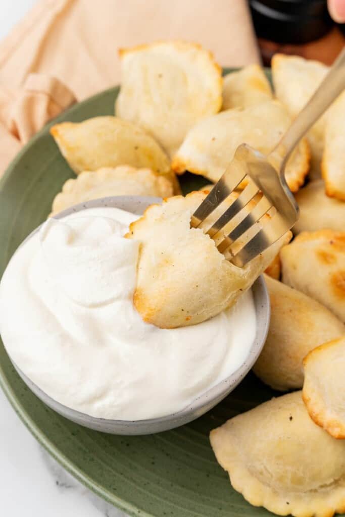 pierogi being dipped into sour cream