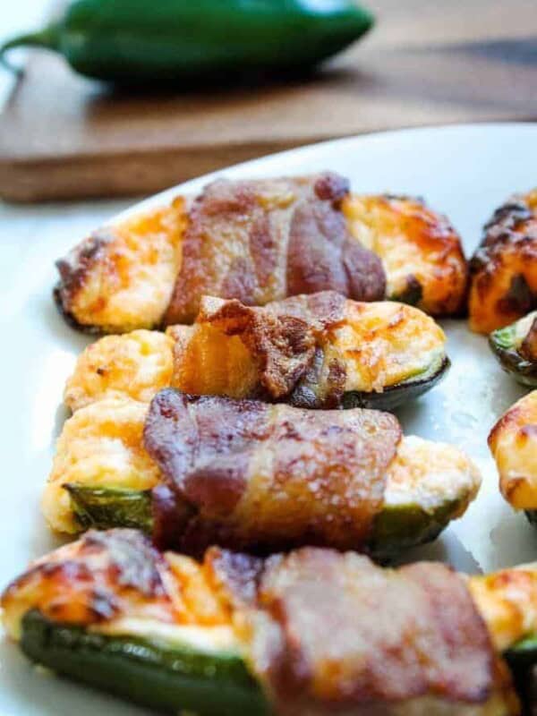 Air Fryer Bacon Jalapenos on a white plate with jalapeno pepper in background