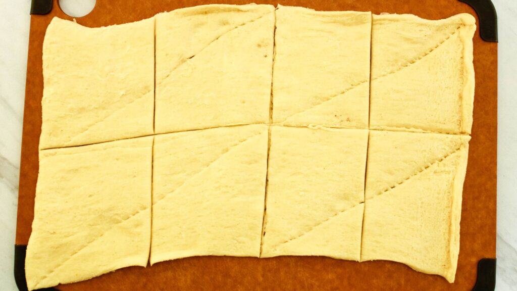 Crescent roll dough cut into 8 sections on a cutting board.