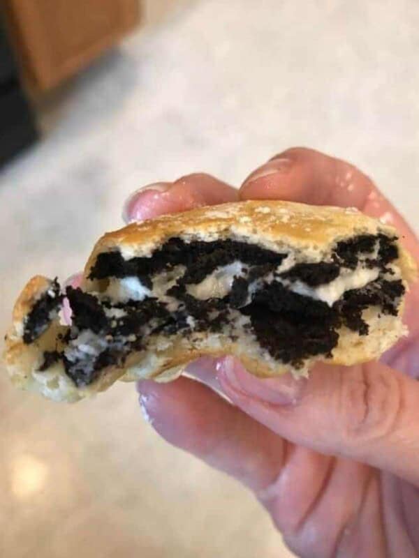 Hand holding an air fryer oreos that has been bitten into so you can see the oreo in the middle.