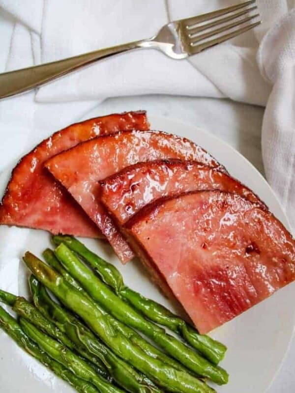 Ham Steaks with Green Beans on a white plate with fork over top of plate