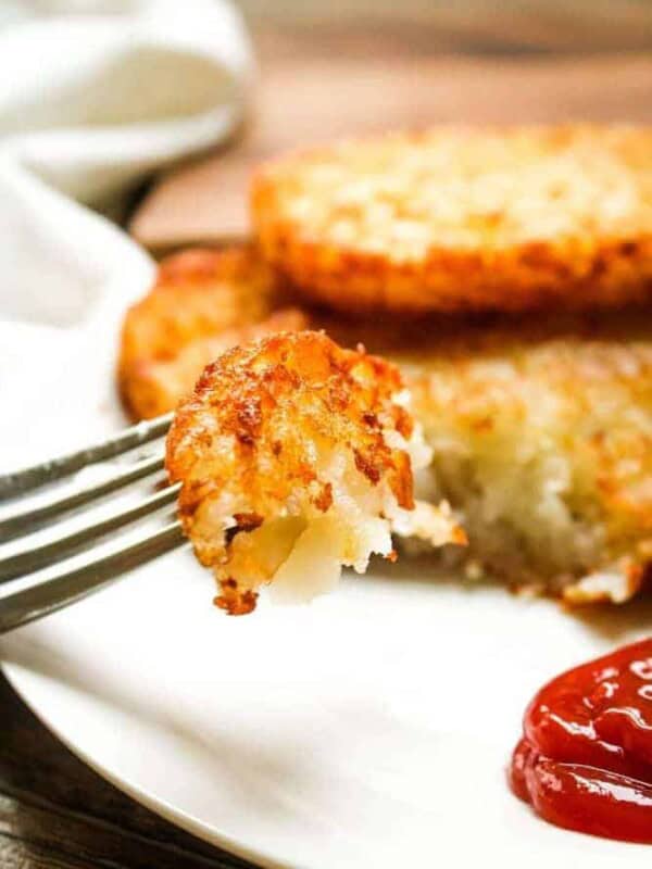 Closeup of a bite of crispy air fryer hash brown patties on a fork with ketchup to the side