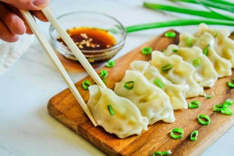 Instant Pot Pot Stickers on a cutting board with chopsticks about to pick up one