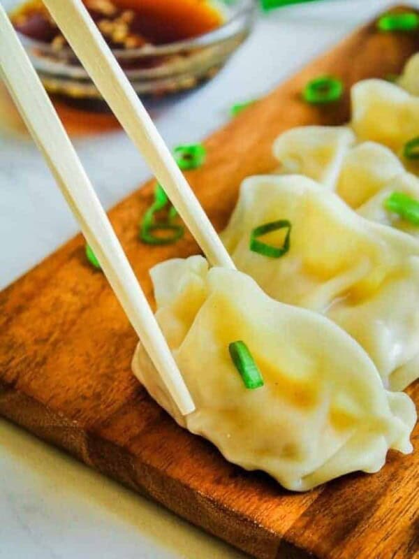 Potstickers on brown cutting board with chopsticks picking up one