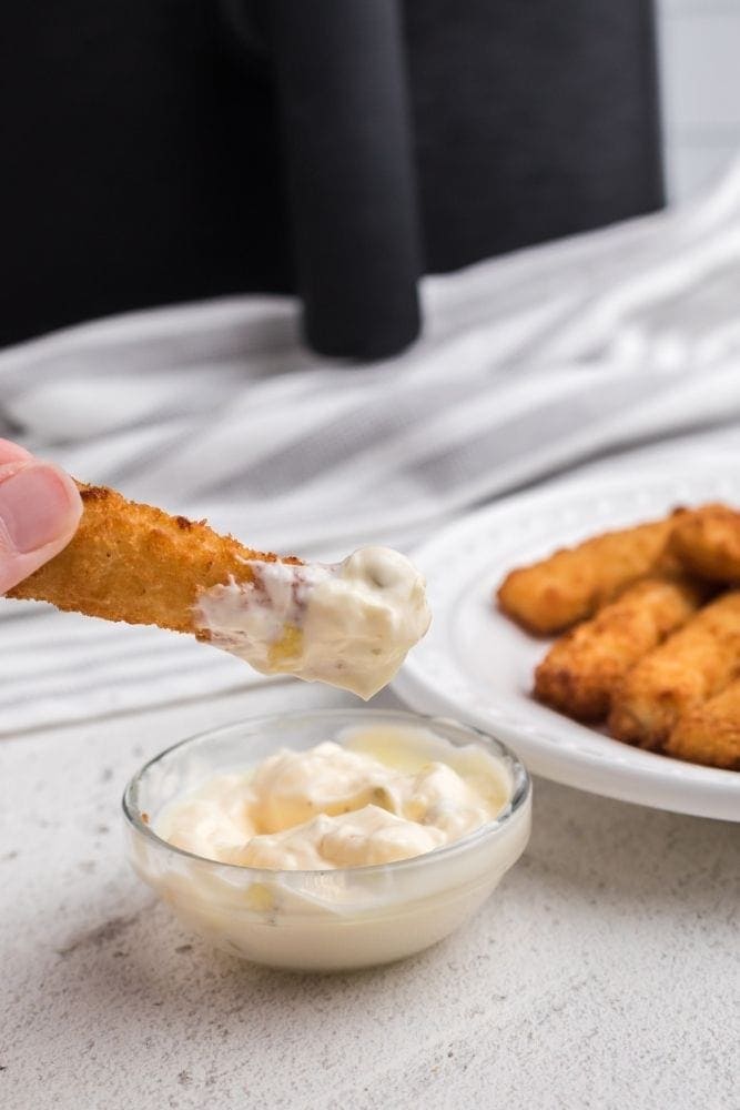 Fish stick with tartar sauce on it with tartar sauce bowl