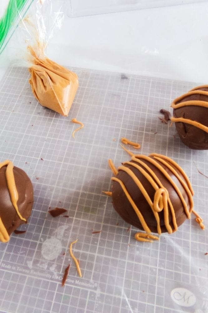 Hot Cocoa Bombs with peanut butter drizzld on top with piping bag in background