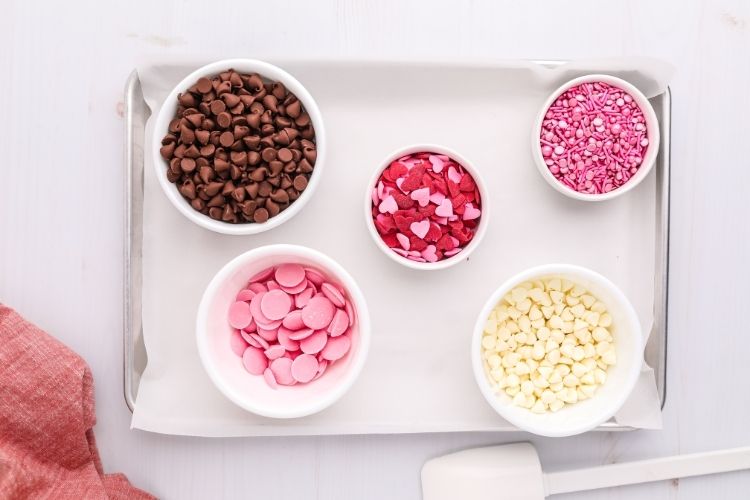 Ingredients for Valentines Day Chocolate Bark on bowls on a cookie tray with parchment paper