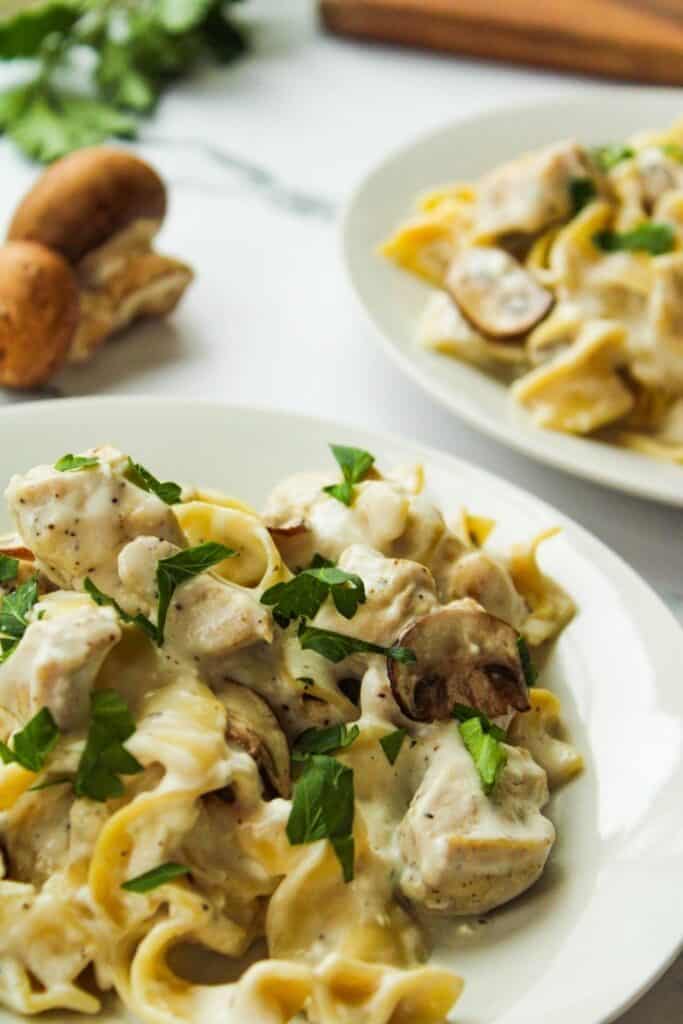 Pressure cooker Chicken Stoganoff on a white plate with another plate full in the background and fresh mushrooms