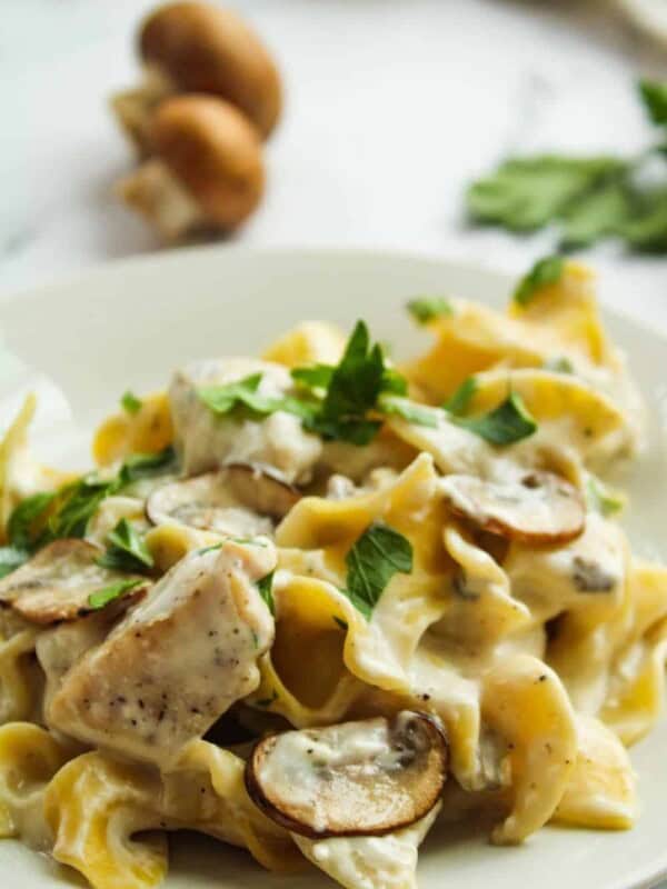 instant Pot Chicken Stroganoff on a white plate with fresh mushrooms in the background