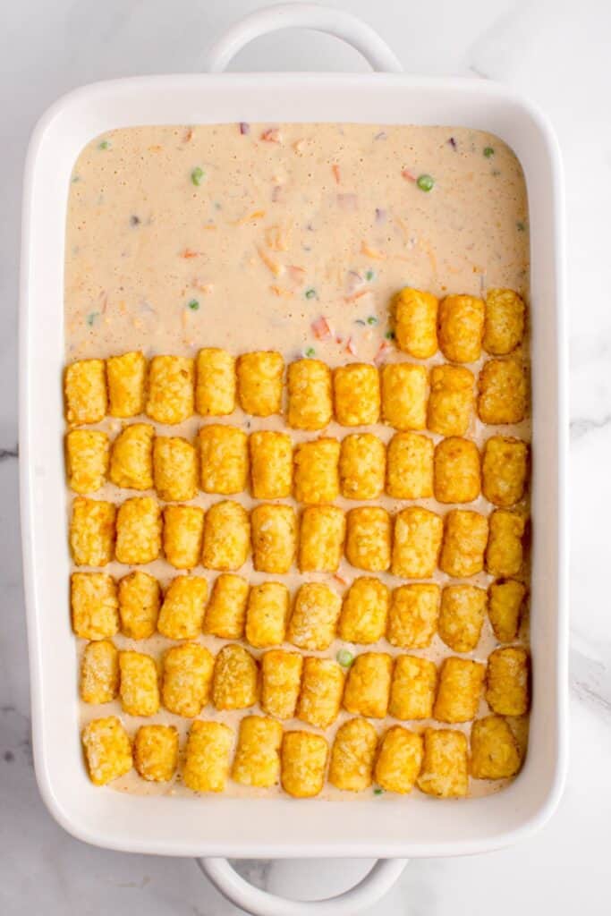 Tater tots being placed in rows on top of the egg mixture in a casserole dish to make the tater tot breakfast casserole.