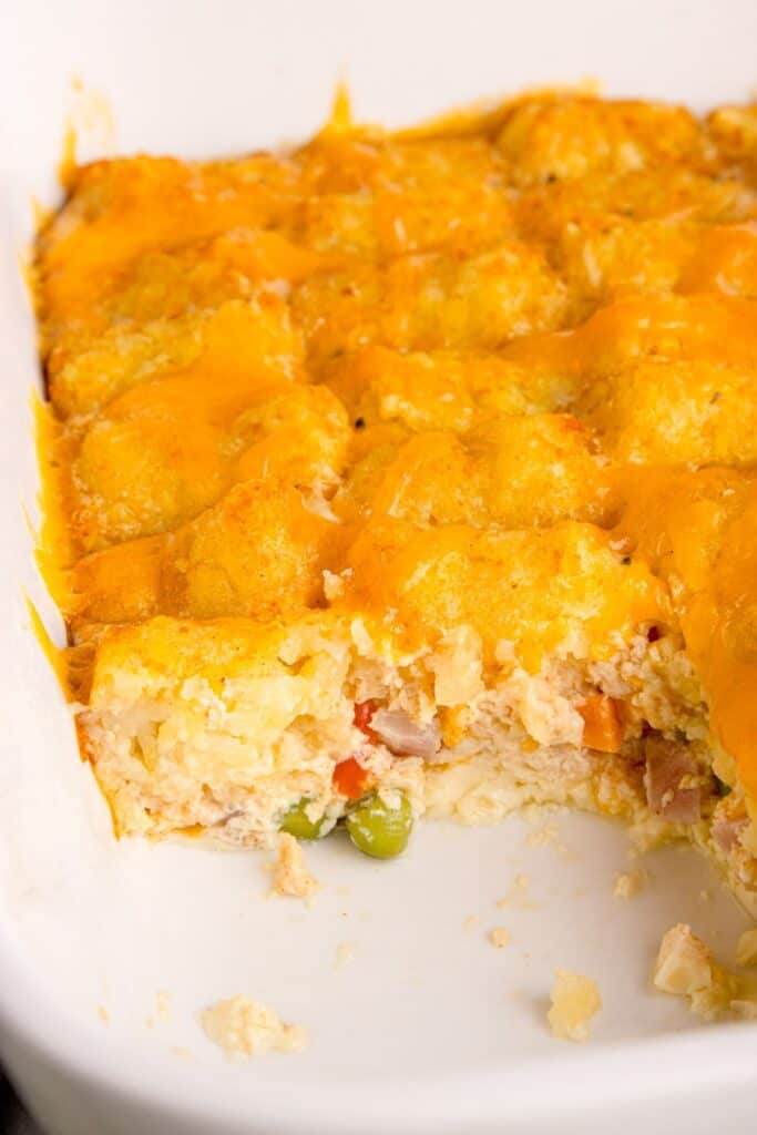 A close up of the baking dish with a slice of the tater tot casserole without meat missing so you can see inside the casserole.