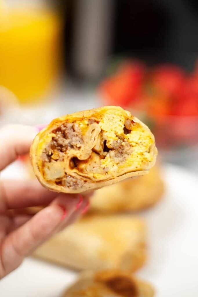 Hand holding half of the cooked breakfast burrito