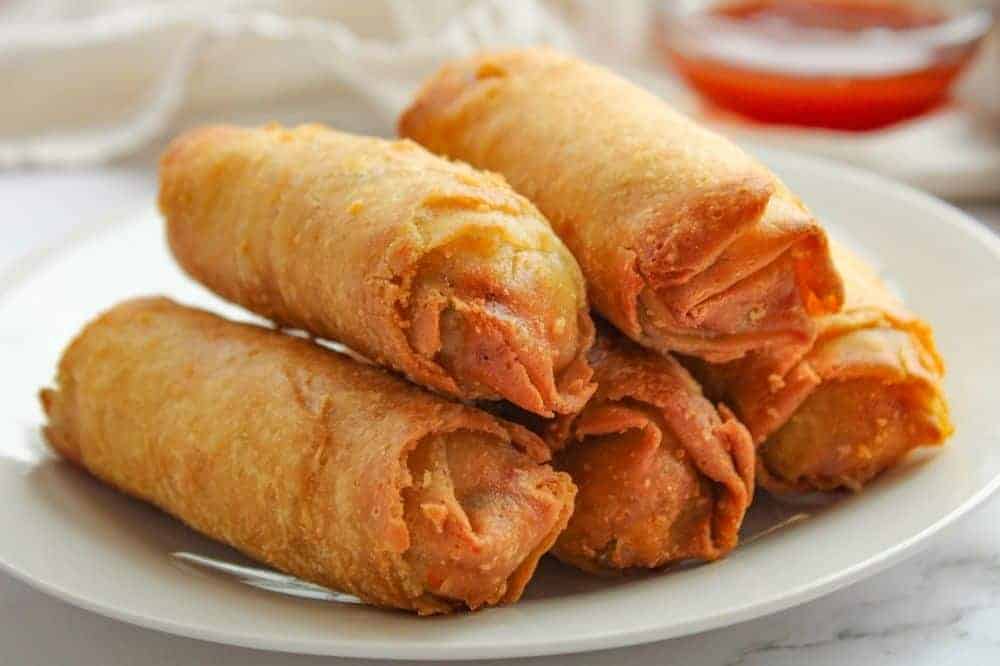 Air Fryer Egg Rolls on a white plate with sauce in a bowl in the background