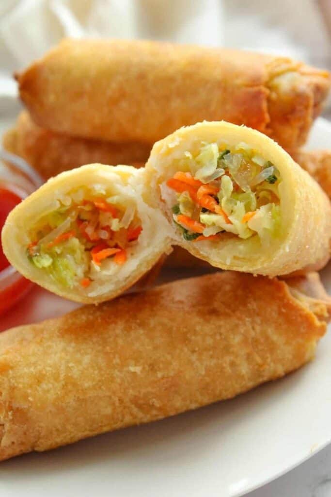 Air Fryer Egg Rolls on a white plate with one cut in half showing the inside
