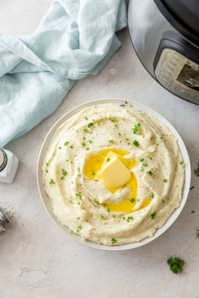 Overhead shot of Instant Pot Mashed Potatoes with Garlic in a bowl with melted butter and Instant Pot in the corner