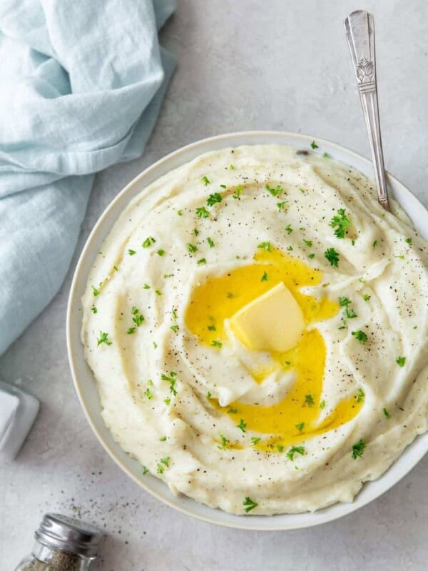 Instant Pot Garlic Mashed Potatoes with sour cream in a white bowl with butter melting on top and a spoon inside the bowl