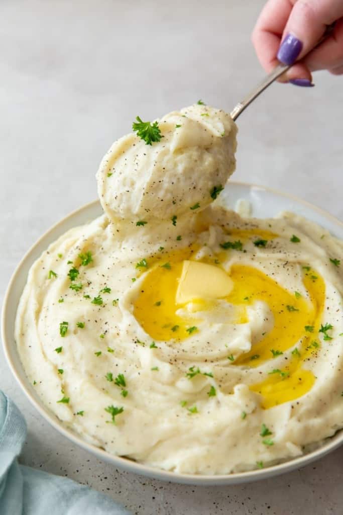 Instant Pot Garlic Mashed Poateos in a bowl with butter melting in it and spoonful of mashed potatoes being taken out