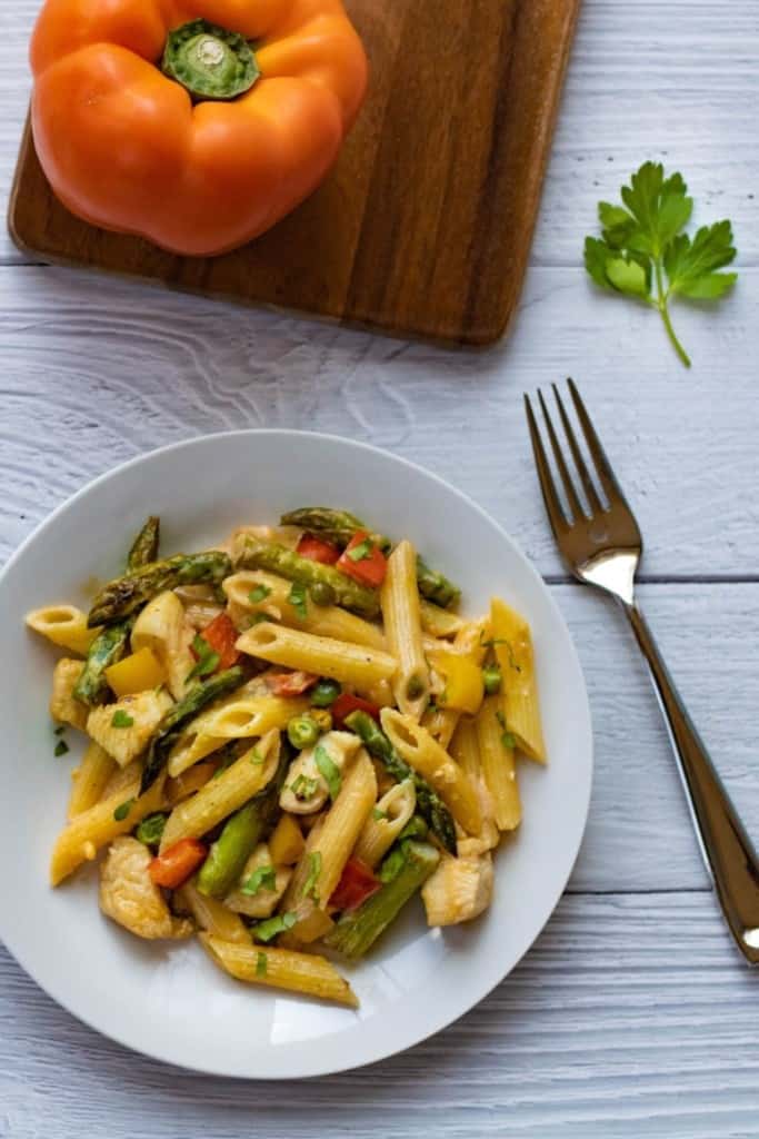 Chicken Chipotle Pasta on a white plate with a fork and orange pepper in the background