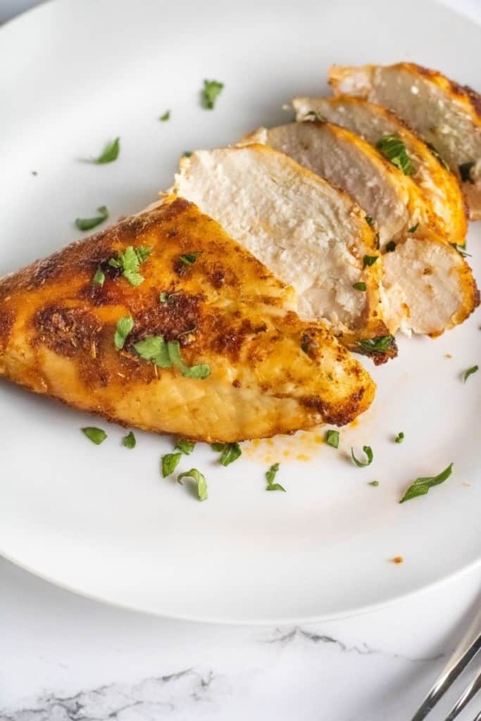 Sliced air fryer chicken breasts on a white plate garnished with parsley