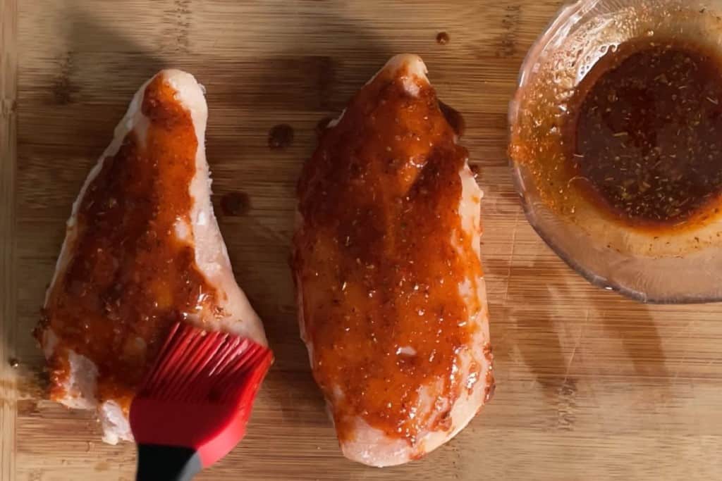 Frozen chicken being basted with spices and oil