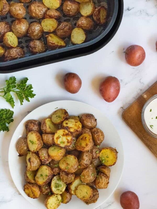 Air Fryer Ranch potatoes on a white plate with more in a square air fryer basket