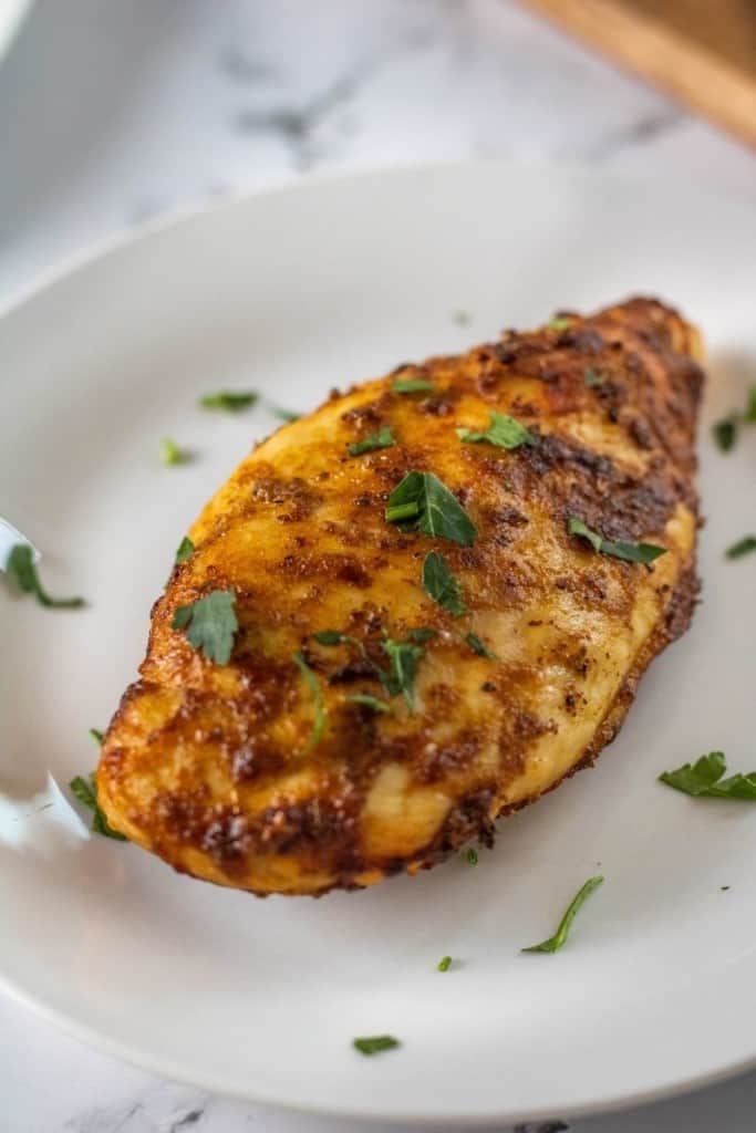 Whole Air Fryer Chicken Breast cooked from frozen on a white plate garnished with parsley