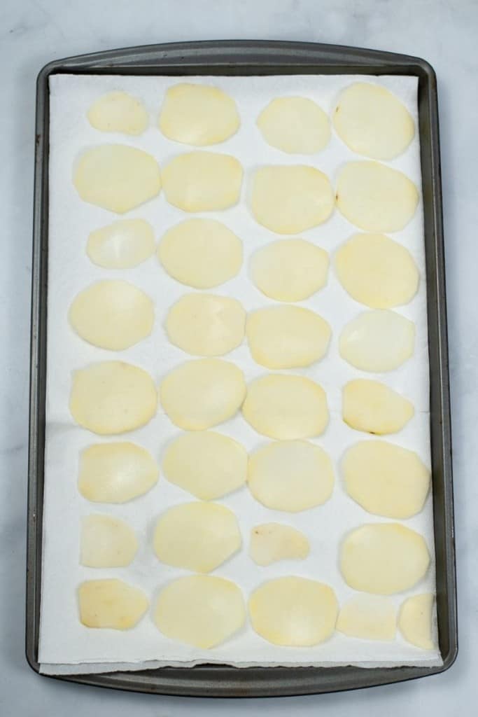 Potato chips drying on a baking sheet on top of paper towel