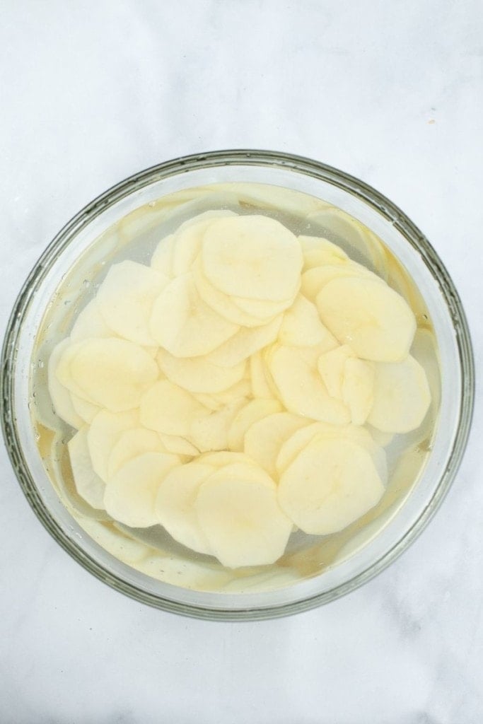 Sliced potato chips soaking in water inside a bowl